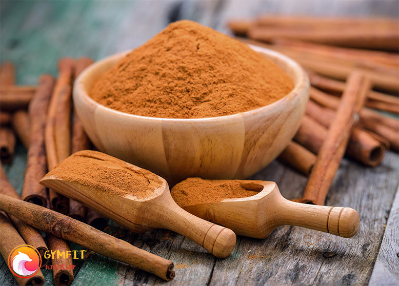 یک ظرف چوبی پر از پودر دارچین و چوب های دارچین در کنار ظرف
